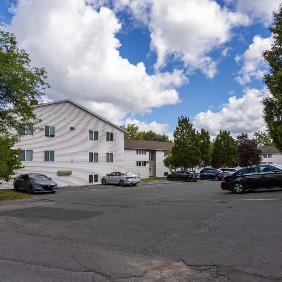 Three-story building between trees, with parking at Brook Manor Apartments, Syracuse NY