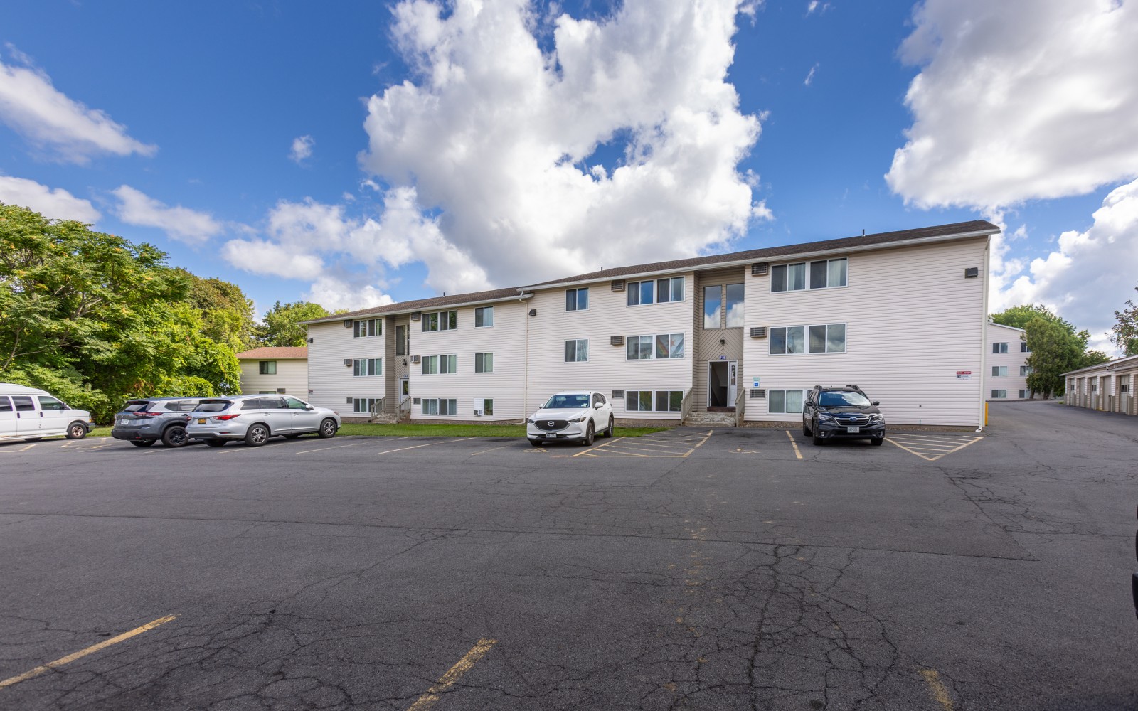 Apartment building and parking lot under a blue sky at Brook Manor Apartments, Syracuse NY
