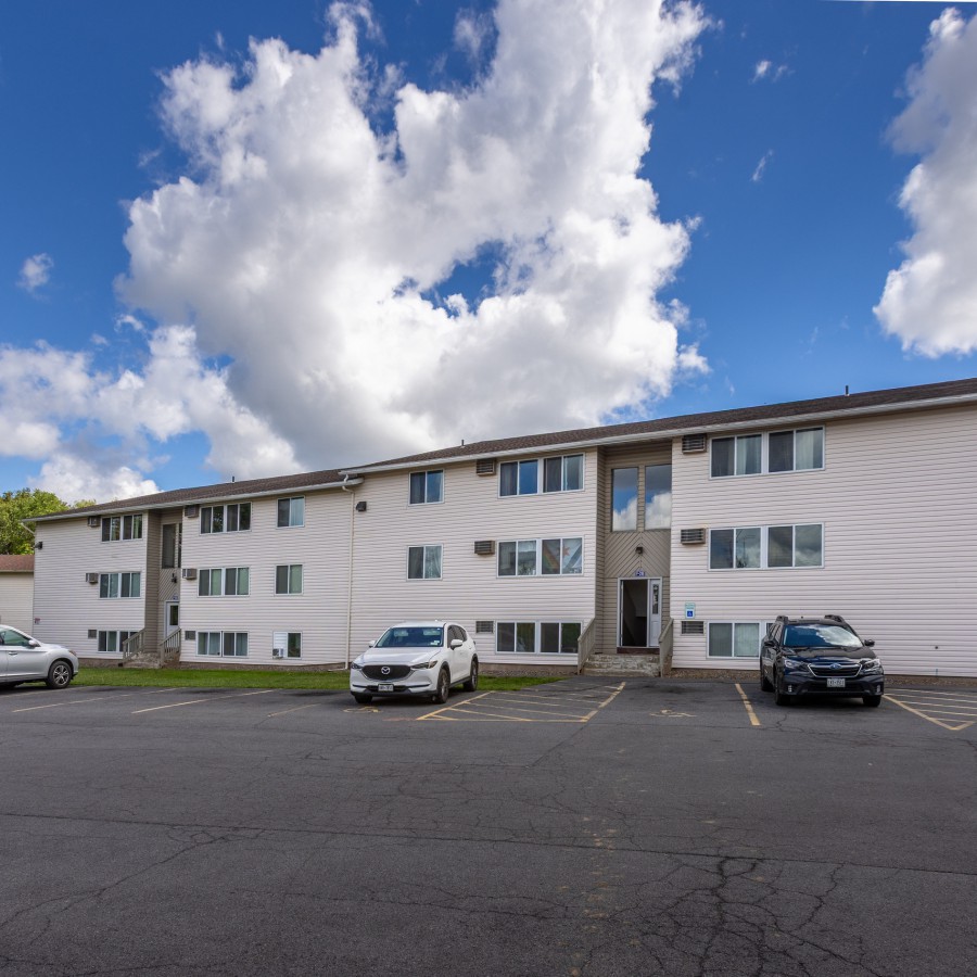 Apartment building and parking lot under a blue sky at Brook Manor Apartments, Syracuse NY