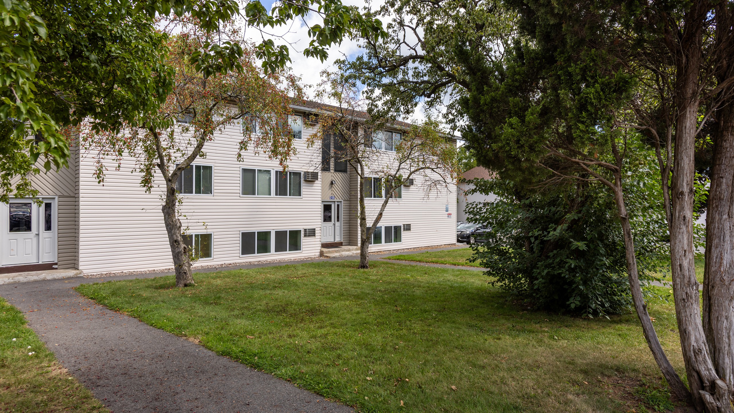 Apartment building with a walkway across the lawn at Brook Manor Apartments, Syracuse NY