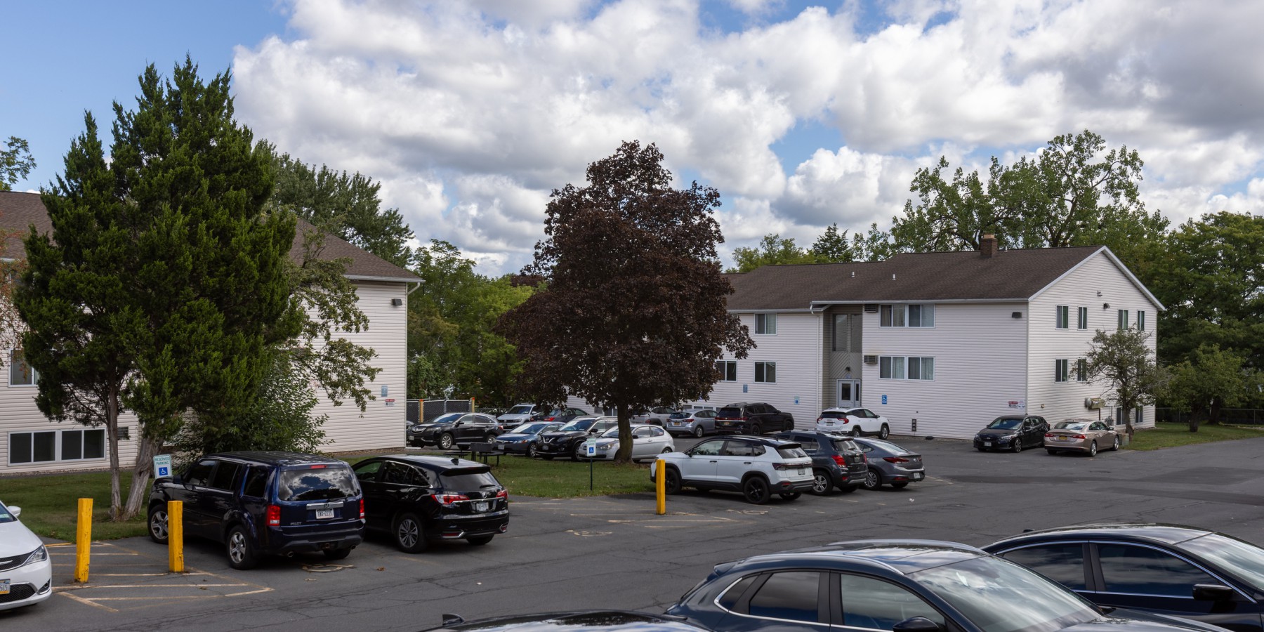 Apartment buildings among trees, with resident parking at Brook Manor Apartments, Syracuse NY