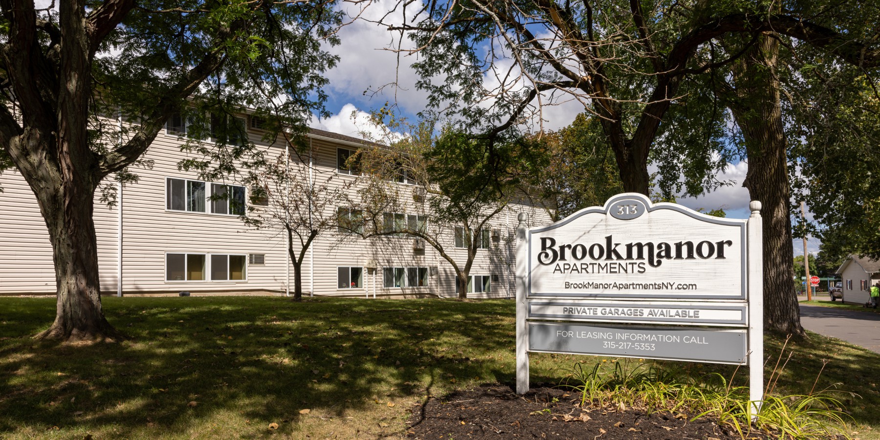 Brook Manor entrance sign on the lawn under shade trees at Brook Manor Apartments, Syracuse NY